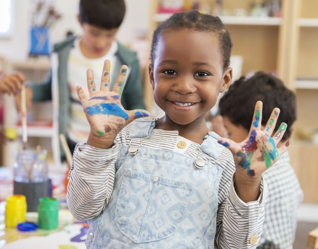Smiling child with paint-covered hands in a classroom, symbolizing school-related laundry mess.