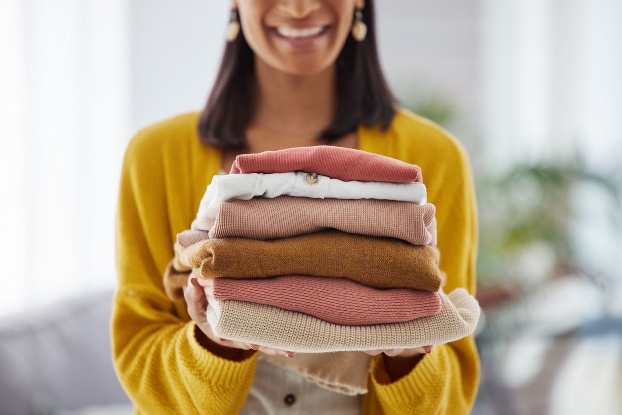 Smiling woman holding a neatly folded stack of clean laundry in a bright, cozy home environment.