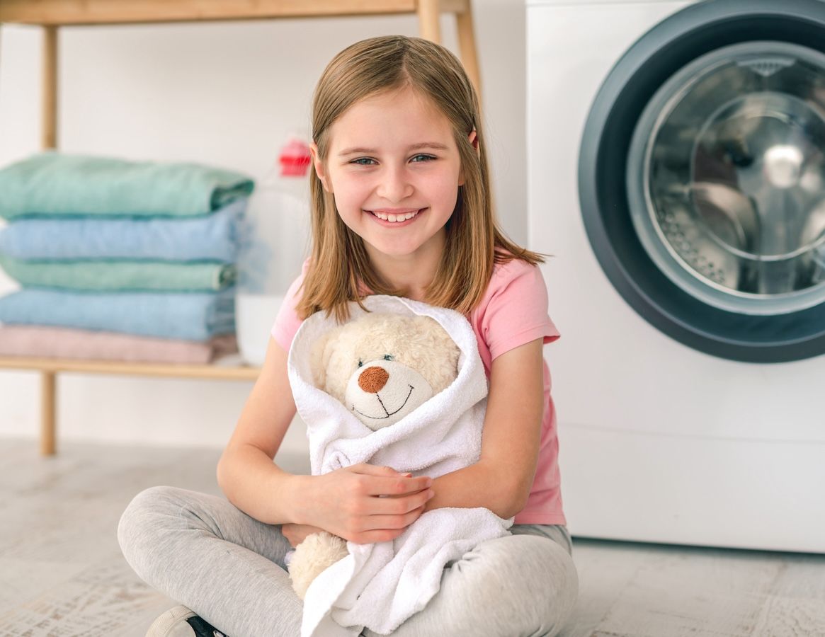 Happy little girl hugging teddy bear in towel after washing in the washing machine.