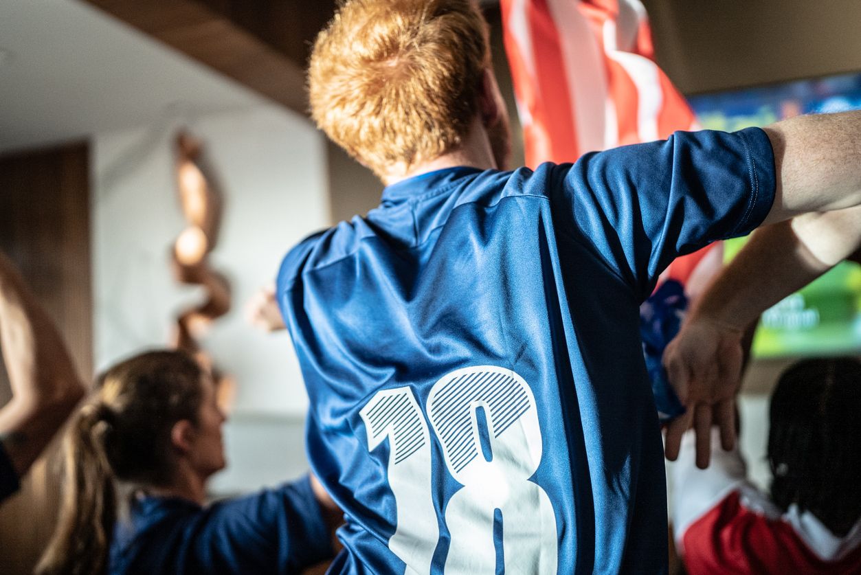 Man wearing a clean football jersey watching TV after it has been washed by Loads of Clothes Delivery.