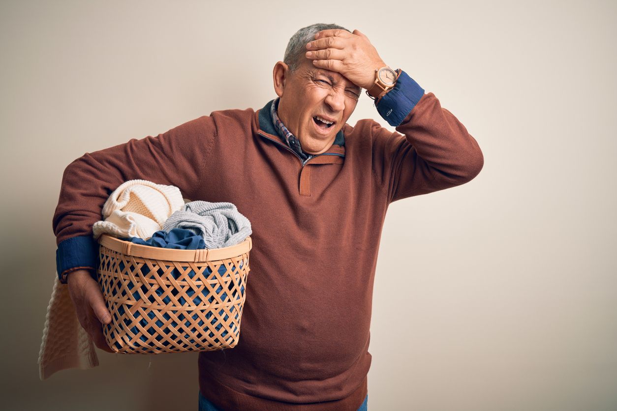 Senior adult male holding basket of dirty laundry looking stressed