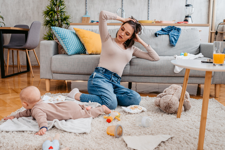 Mom with baby surrounded mess of items and baby laundry, showing that baby laundry is no joke for busy parents